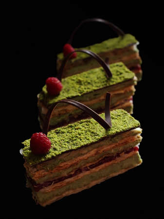 Pistachio puff pastry cake with raspberries and chocolate on black backgroundの写真素材
