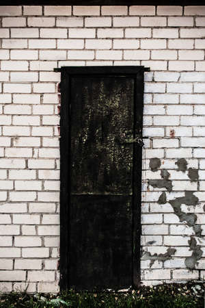 Old spooky dark black wooden door with a lock in white brick wall with spotsの写真素材
