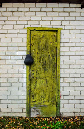 Old greenish yellow wooden door with a lock in white brick wall with green grass bottomの写真素材