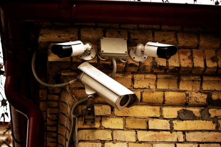 Three white video cameras on yellow brick wall on building corner