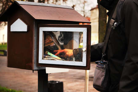 Man taking a book in a small park outdoor library with books for exchange in autumnの写真素材