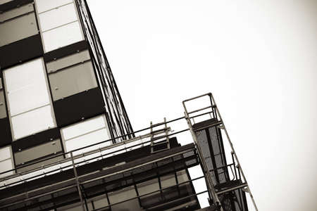 Modern building construction site with wooden ladder on white sky background in grayscale