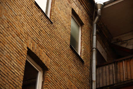 Closed windows in brick wall with drainage pipe and balcony