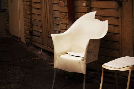 White broken plastic armchair in yard on wooden wall with doors backgrundの写真素材