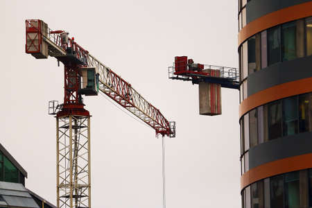 Construction cranes working on modern building on white sky background