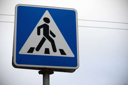 Blue road crossing sign on white sky background with wiresの写真素材