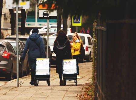 Two women with bags on wheels walking along a street in autumnのeditorial素材
