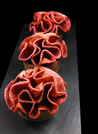 Red fruit apple and cherry leather ruffled dessert tarts on black vulcanic plate on black backgroundの写真素材