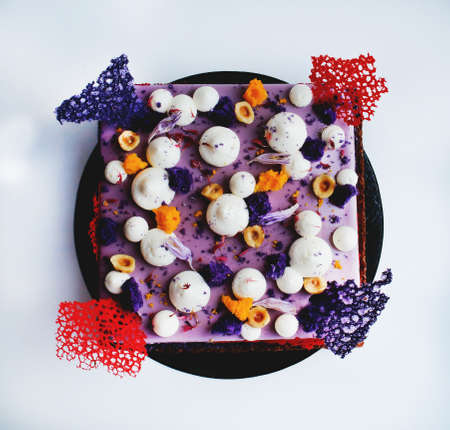 Colorful square purple cake with colored crepe lace decorations, hazelnuts and whipped cream...
