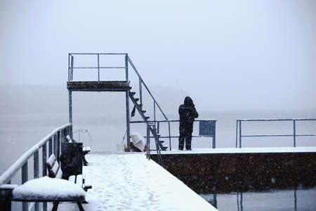 Old fisherman with a pole fishing in winter lake standing on pier