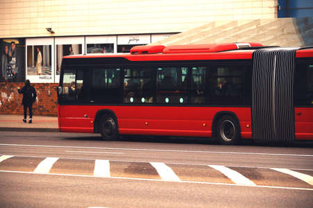 Red long city bus standing on street near a shopping centerのeditorial素材
