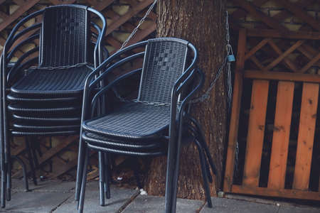 Black cafe outdoor weaved chairs stacked and chained to a treeの写真素材