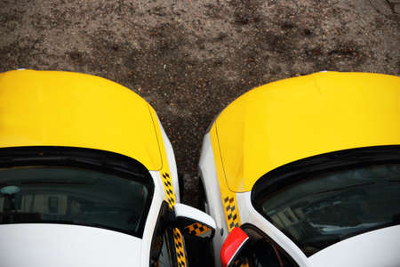 Two yellow taxi cars standing together with dark front windows