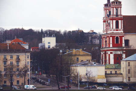 Vilnius town street with leafless trees, cars and red church in warm winter without snow in Lithuania, Europeのeditorial素材