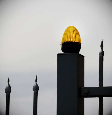 Orange light bulb on black metal fence on white sky backgroundの写真素材