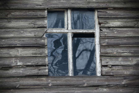 Old white frame wooden window in wooden wall with dirty broken glassの写真素材