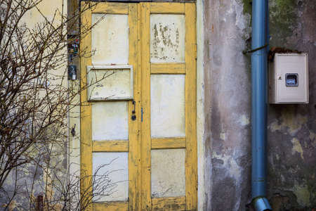 Old locked yellow wooden door with electricity box, water pipe and door bell buttons