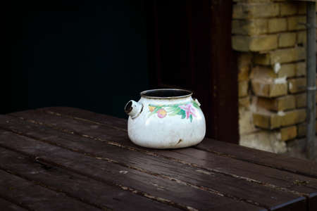 Old broken kettle standing on wooden table outdoors