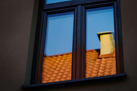 Modern architecture dark grey building window with blue sky and red roof with chimney reflection