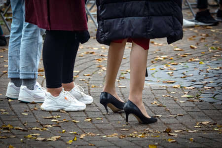 Different womens legs in different shoes standing on pavement with fallen yellow leavesの写真素材
