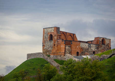 Old red brick castle building on green hill on dull evening sky background with clouds