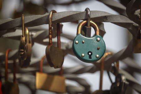 Green padlock hanging on crooked iron bar with many small padlocks on backgroundの写真素材