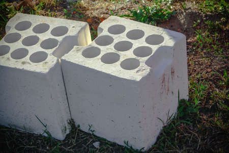 Two white big bricks with round holes lying on ground in forest on tiny green grass side view