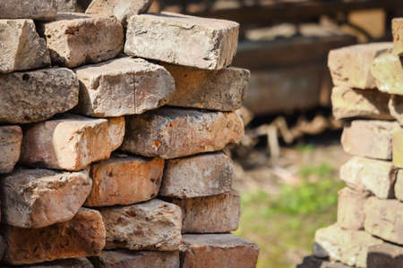 Brick wall corner with sticking out old red bricks and visible green grass on the background