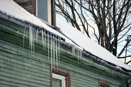 Row of icicles ahnging on roof edge of green wooden house