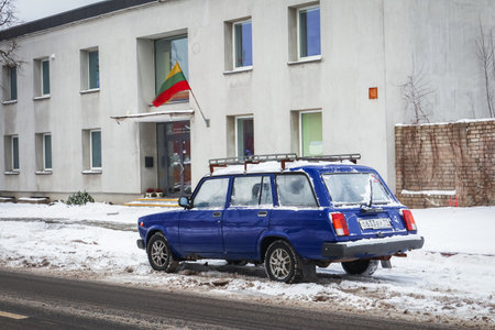 Vilnius, Lithuania - 12 2021: Old Soviet Union blue moskvich car in good state on snowy road near a building with Lithuanian flagのeditorial素材