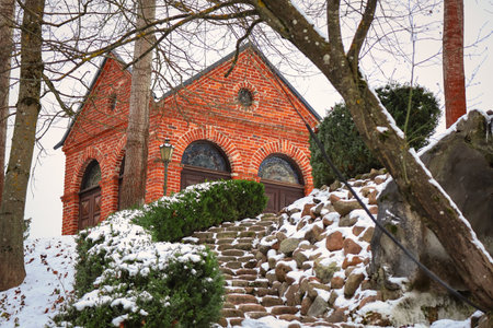 Small red brick old house on hill visible from leading down stairs with hedges covered in snow in winterの写真素材