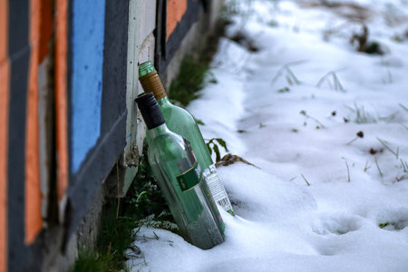 Two green glass empty alcohol bottles standing in snow near kiosk wallのeditorial素材