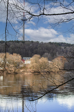 River flow with reflections of blue sky and trees in spring with visible Vilnius television tower on the backgroundの写真素材