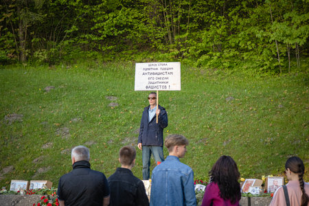 Vilnius, Lithuania - May 09 2023: Antakalnio cemetery Victory Day gathering on a place of demolished memorial momument to the Soviet Soldiers of WWII with man standing holding a protest bannerのeditorial素材