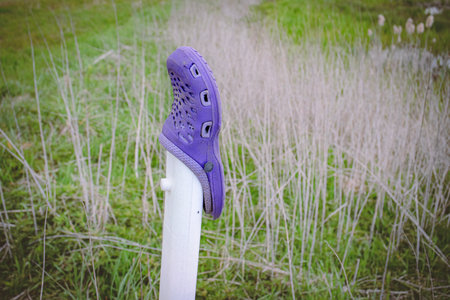 Purple worn and old rubber shoe left on a white road post near sand road in a meadow backgroundの写真素材