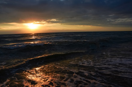 Side view of a big wave under the beautiful orange sunset of the sun going down over the Baltic seaの写真素材