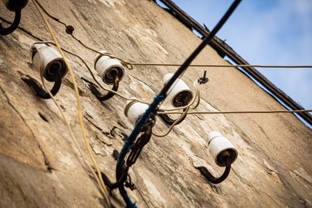 Four white ceramic fasteners for electrical wiring on an old building soht in diagoal with visible white and blue sky over roofの写真素材