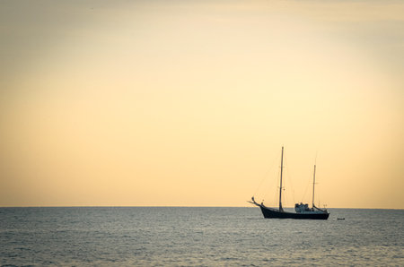 Yacht resting on sea water in sunset light with a tiny still visible plane rising from the nice airportの写真素材