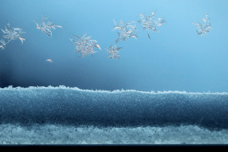 Frost snowflakes painted on window glass and some snow at the bottom in winter cold blue light....