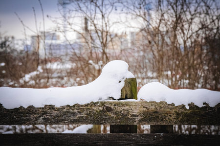 Big fluffy soft snowdrift on a wooden fence on snowy winter day with visible trees and modern buildings on the backgroundの写真素材
