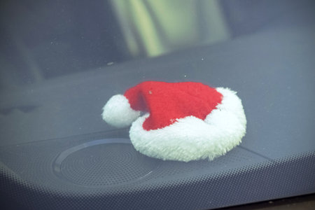 Red Santa's hat lying on a front window of a car behind a dirty glass on blue gloomy dayの写真素材