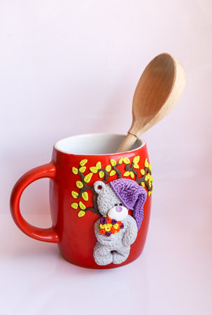 Handmade red ceramic mug with polymer clay bear in knitted hat with small flowers in bouquet under the tree with spoon inside the mugの写真素材
