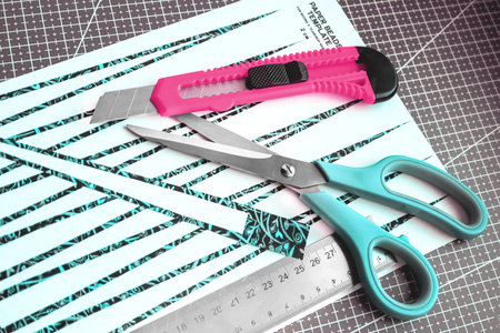 Handmade paper bead templates of green colored floral patterns lying on a cutting mat with pink craft knife and a scissors top viewの写真素材