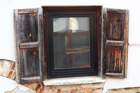 Rustic style aged window with shutters at rural home wall painted white with visible red bricksの写真素材