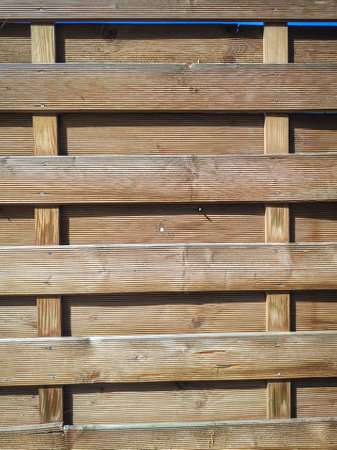 Texture of a wooden plank fence with horizontal and vertical wood strips, brown wooden wall on sunny day backdropの写真素材