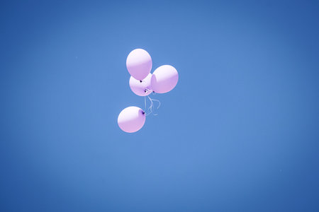 Light pink balloons in blue summer sunny sky flying up and away on blue sky backgroundの写真素材
