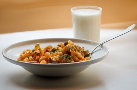 Spiral pasta in sauce with chicken, beans and vegetables covered with dill in a white plate on a kitchen table with metal fork and a glass of milk side viewの写真素材
