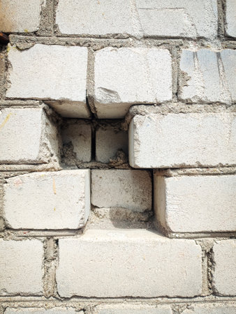 A close-up photo of a weathered white brick wall with a jagged hole in the centerの写真素材