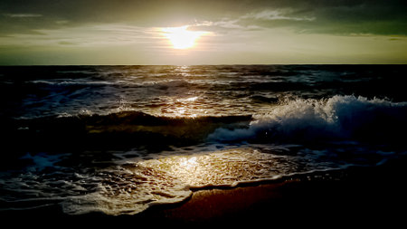 Sunset over seas waves with foam dark landscape with visible sun over waterの写真素材