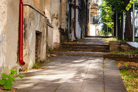 Amazing old narrow street pedestrian pavement path going up along an old building wall on late summer sunny day with green grass and yellow leavesの写真素材